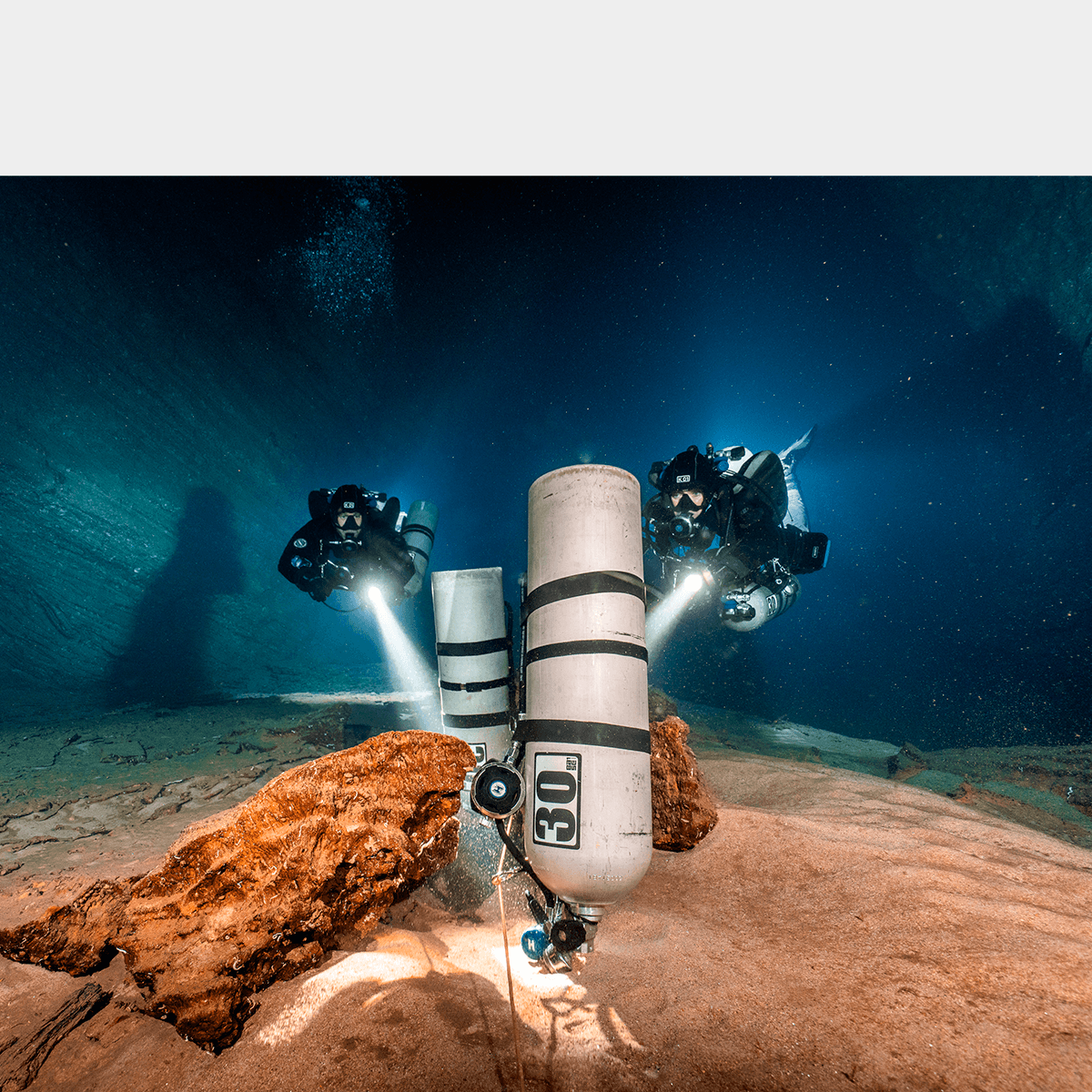 Divers in the cave swimming to staged cylinders